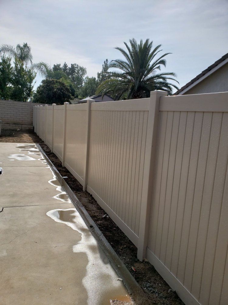 A white fence is sitting on top of a concrete driveway next to a palm tree.
