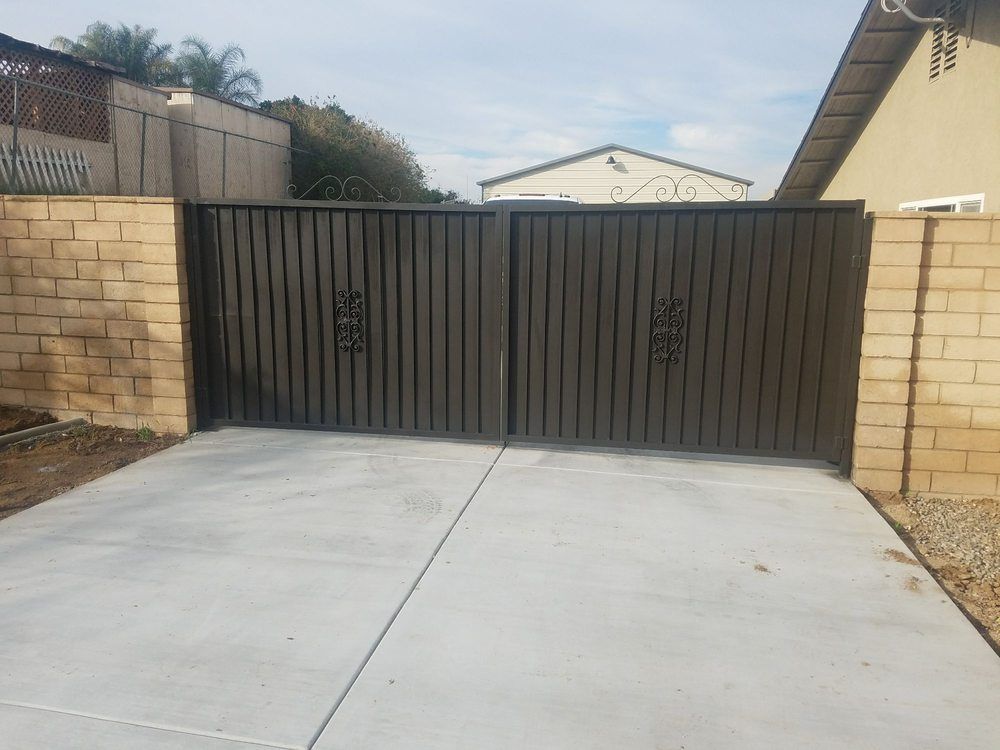 A gate is sitting in the middle of a driveway next to a brick wall.