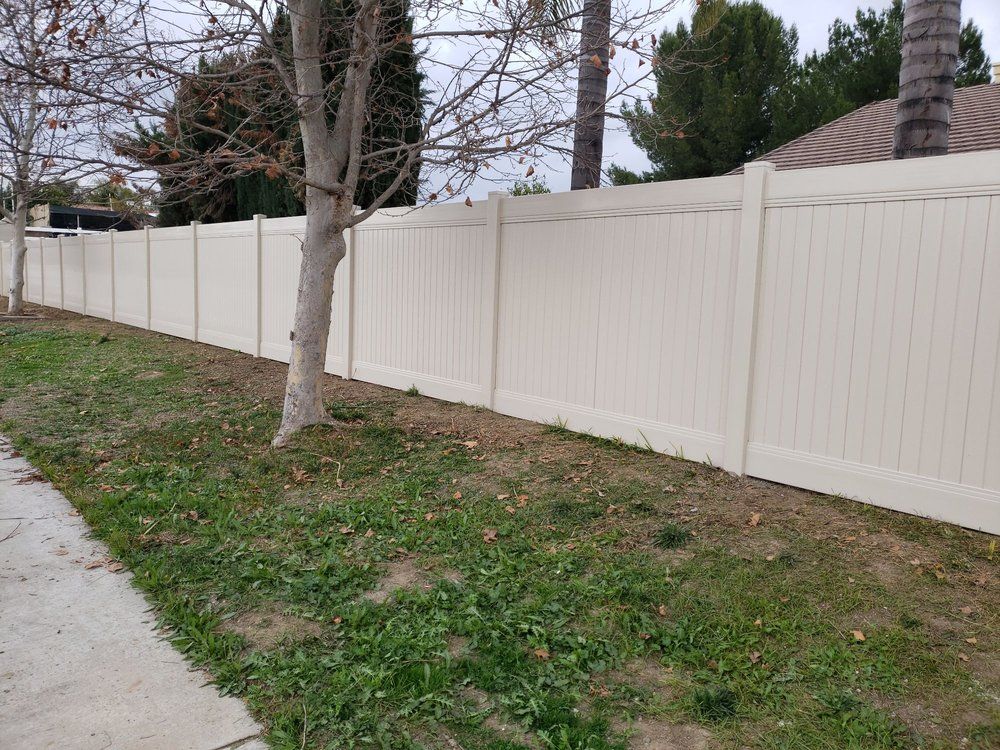 A white fence surrounds a lush green yard next to a sidewalk.