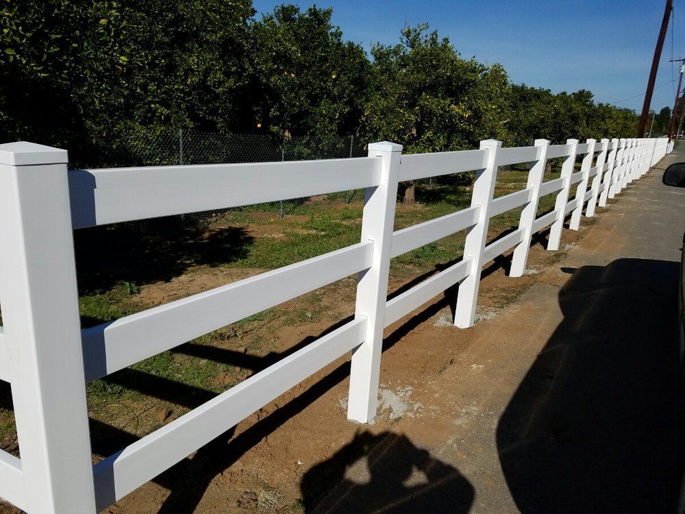 A white fence surrounds a field with trees in the background