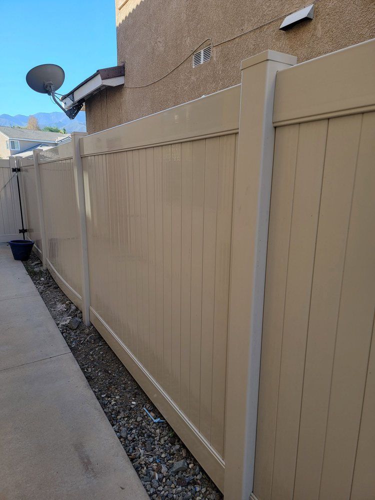 A tan vinyl fence is sitting next to a sidewalk next to a building.