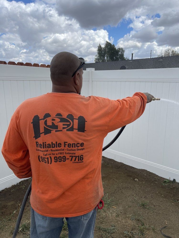 A man in an orange shirt is spraying a white fence with a hose.