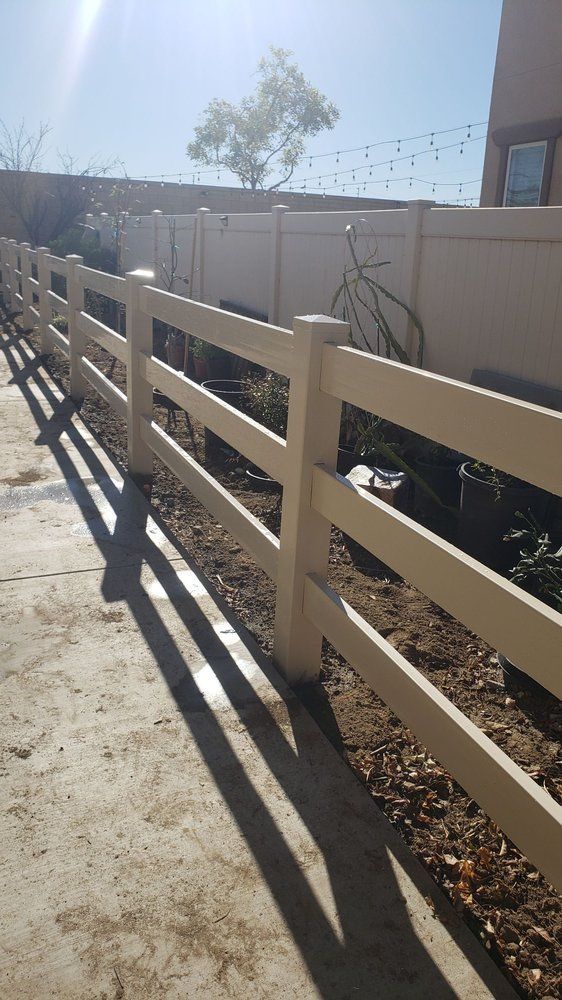 A white fence is sitting on top of a dirt path next to a house.