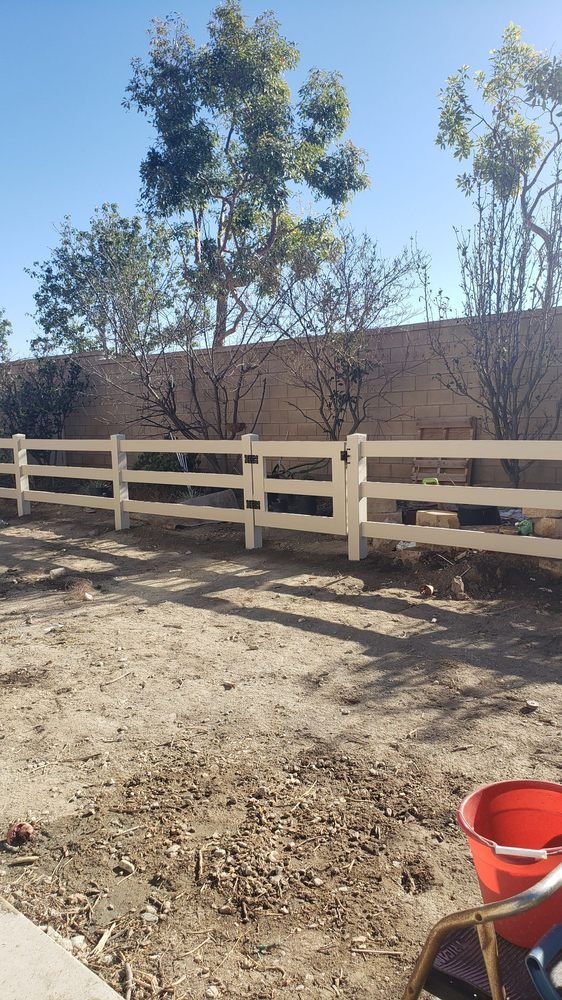 A white fence surrounds a dirt field with trees in the background.