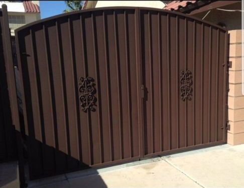 A brown gate with a wrought iron design on it is sitting on a sidewalk.