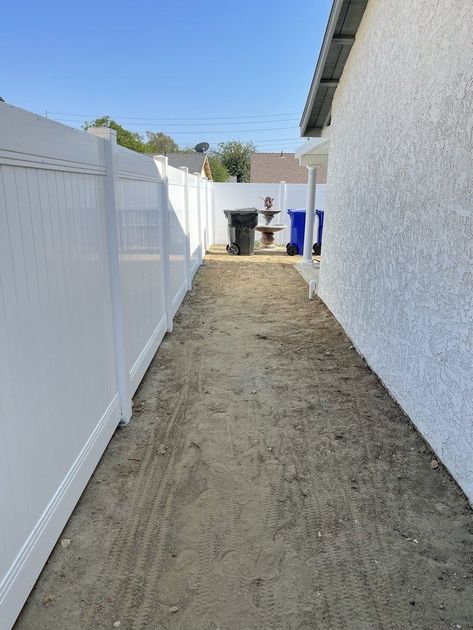 A white fence surrounds a dirt path leading to a house.