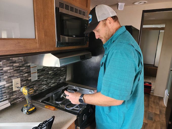 A man in a blue shirt is working on a stove in a kitchen