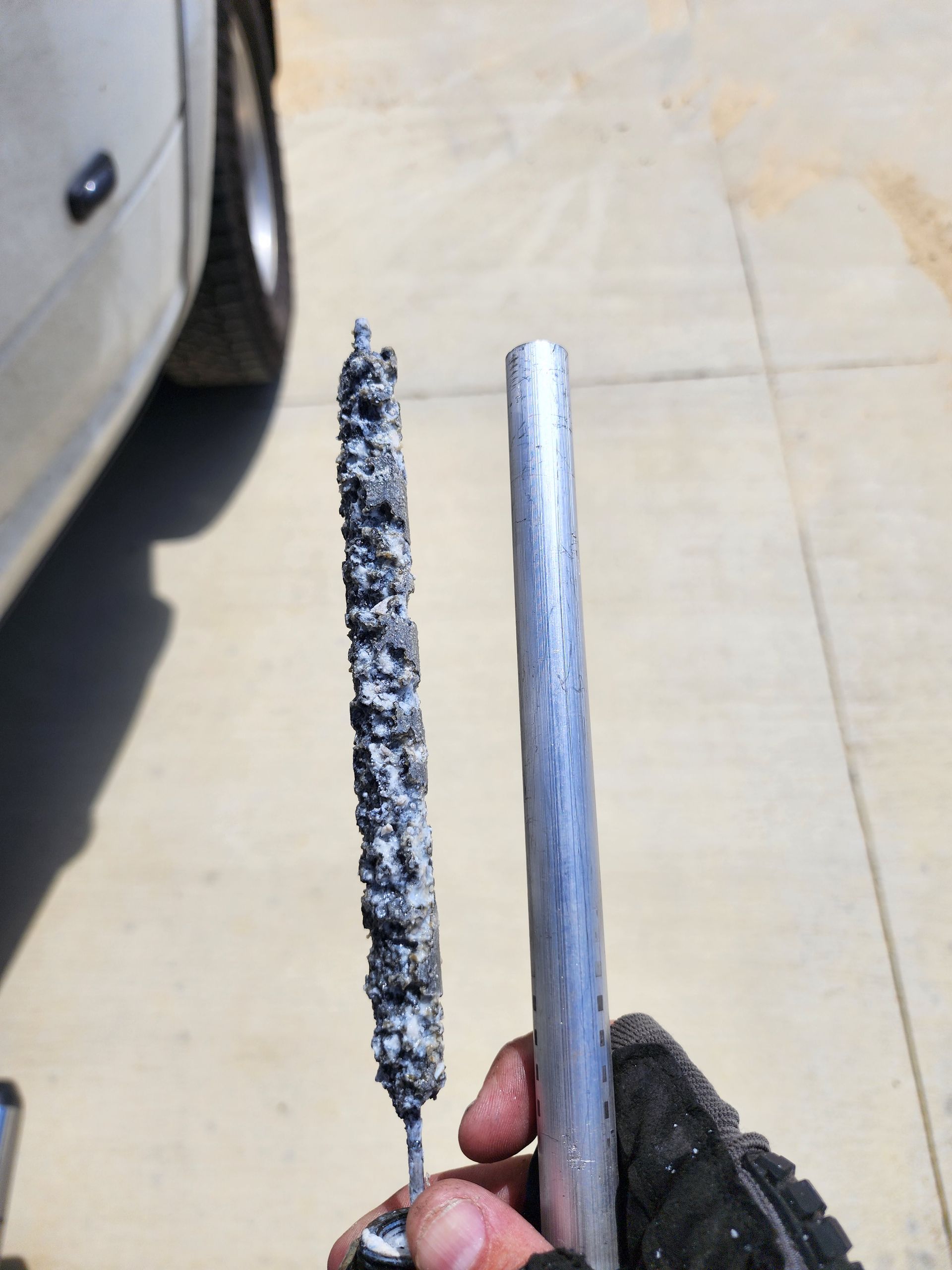 A person is holding a piece of metal with a car in the background