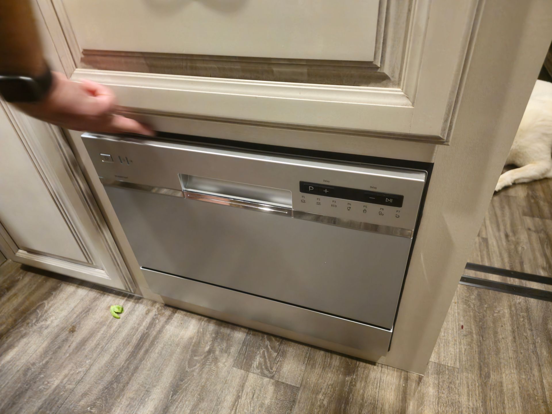 A person is opening a stainless steel dishwasher in a kitchen.
