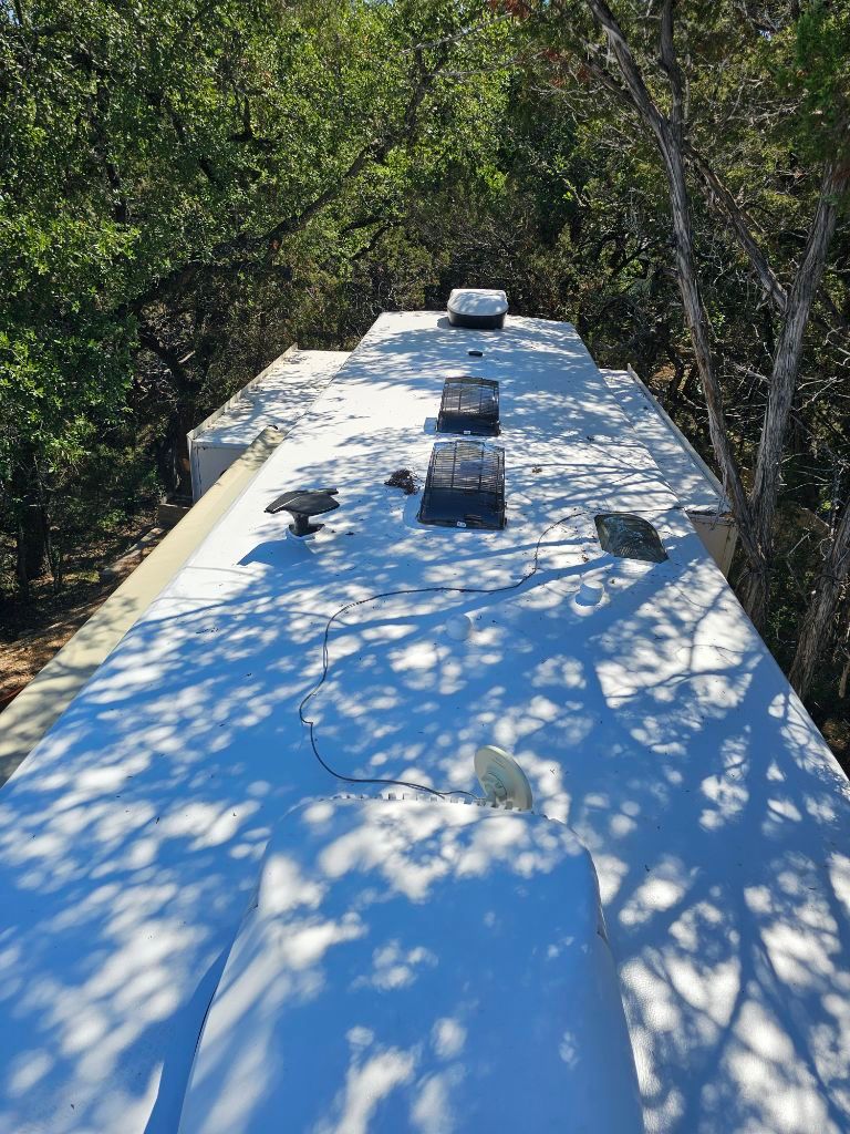 The roof of a rv is covered in snow and trees.