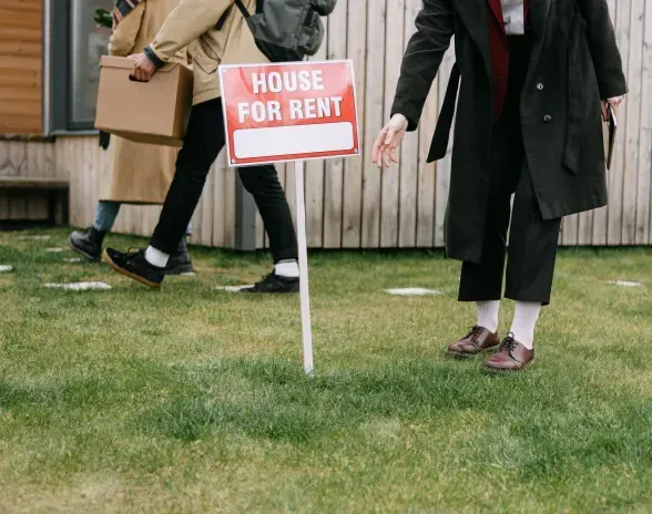 A woman is standing in front of a house for rent sign.