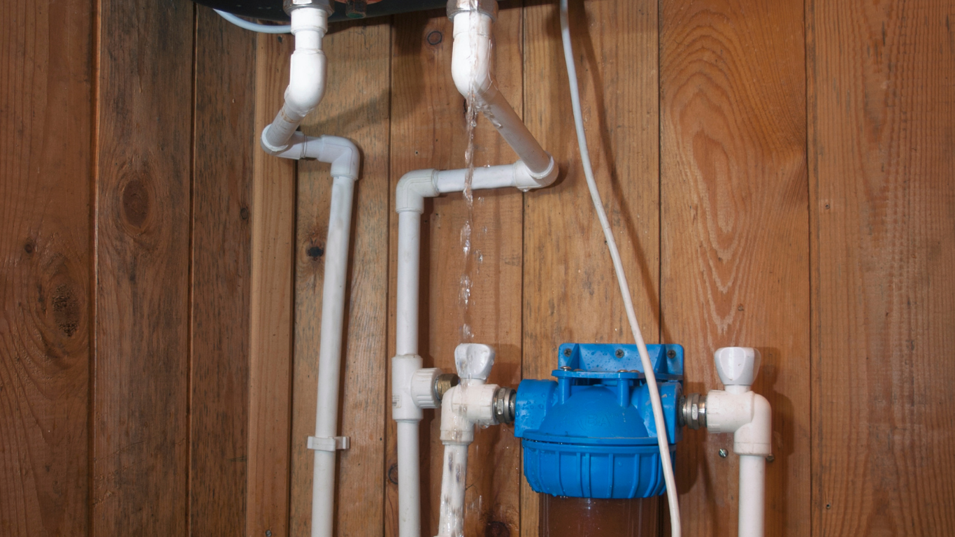 A water filter is hanging from a pipe on a wooden wall.