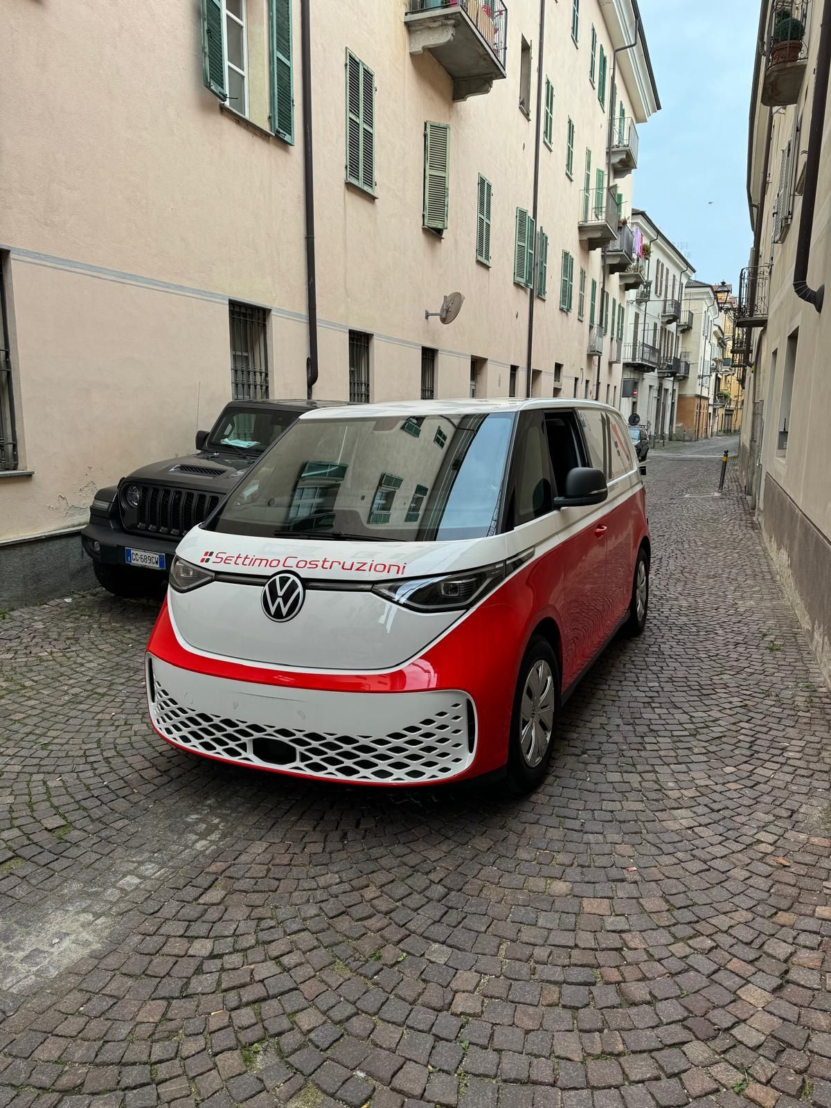 Furgone Volkswagen ID. Buzz rosso e bianco parcheggiato su una strada acciottolata in una città europea.