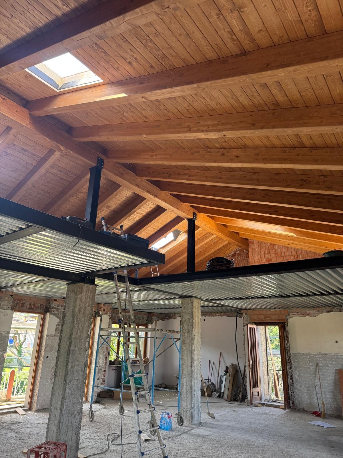 Interno in costruzione con soffitto in legno a vista, travi in ​​metallo e pilastri in cemento.