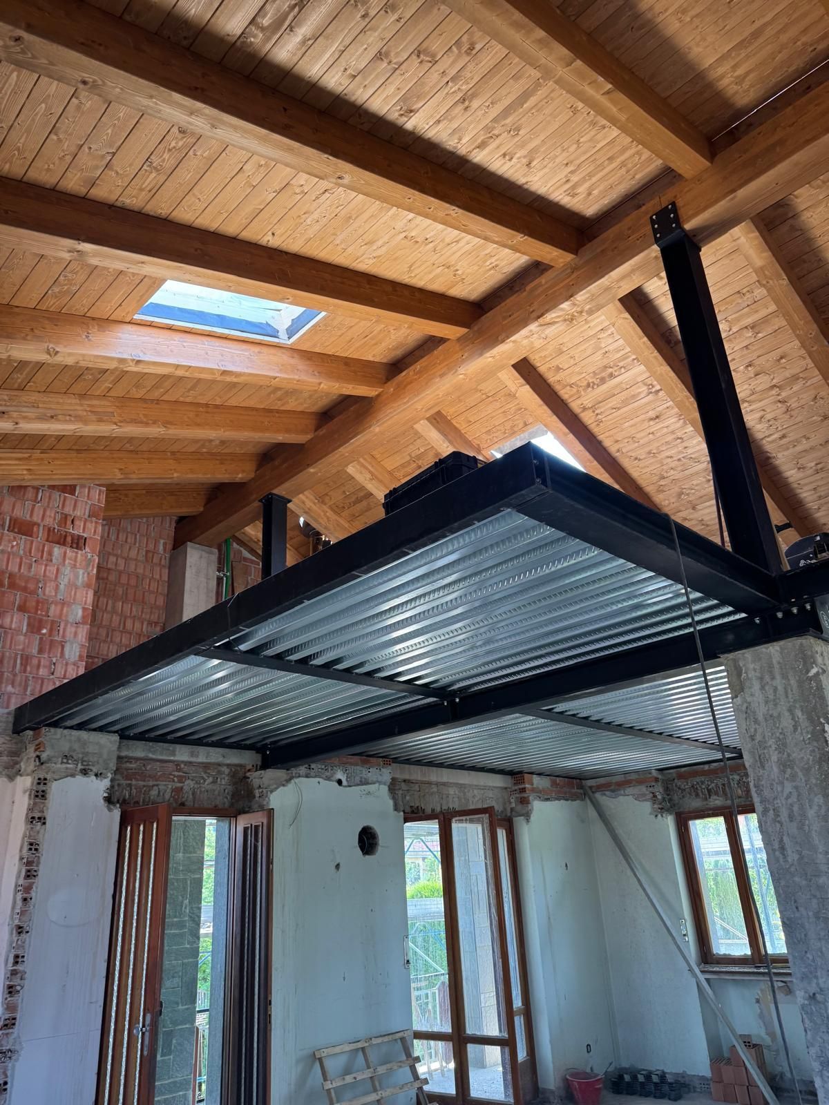 Vista interna di un loft con soffitto in lamiera ondulata, travi in legno e un muro di mattoni.