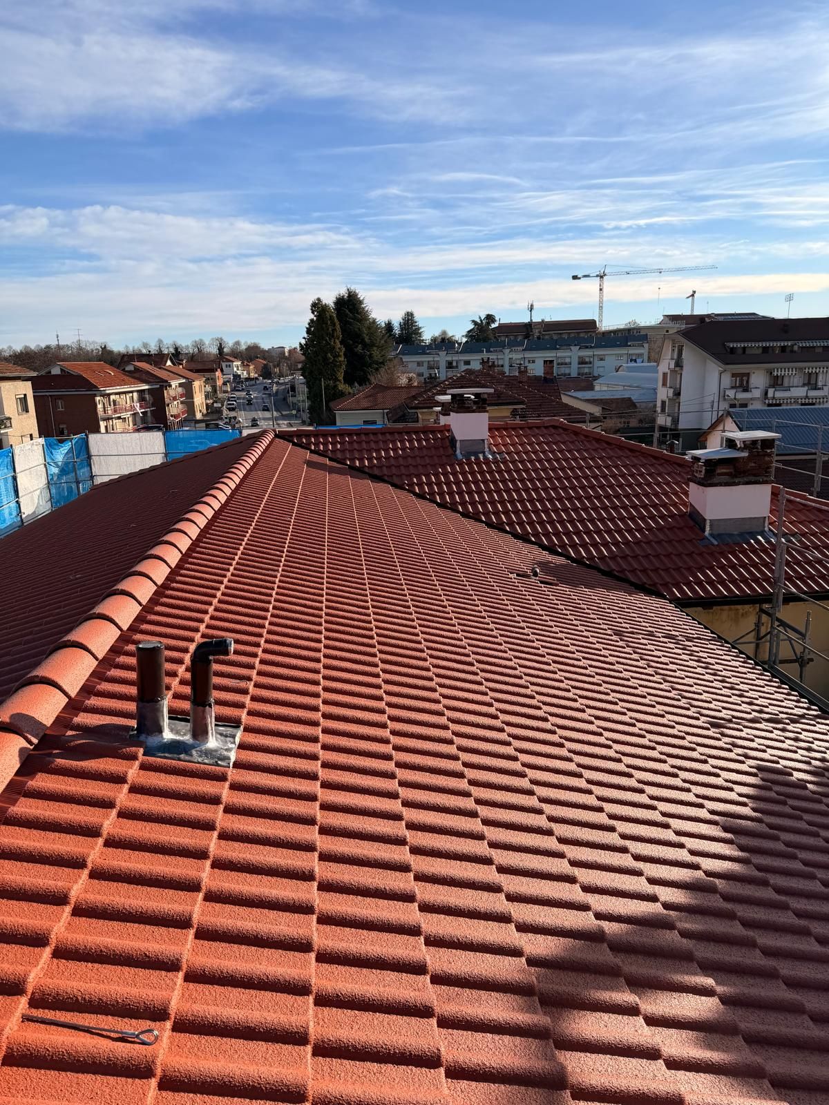 Tetto di tegole rosse con due tubi di metallo contro un cielo azzurro con nuvole sparse.