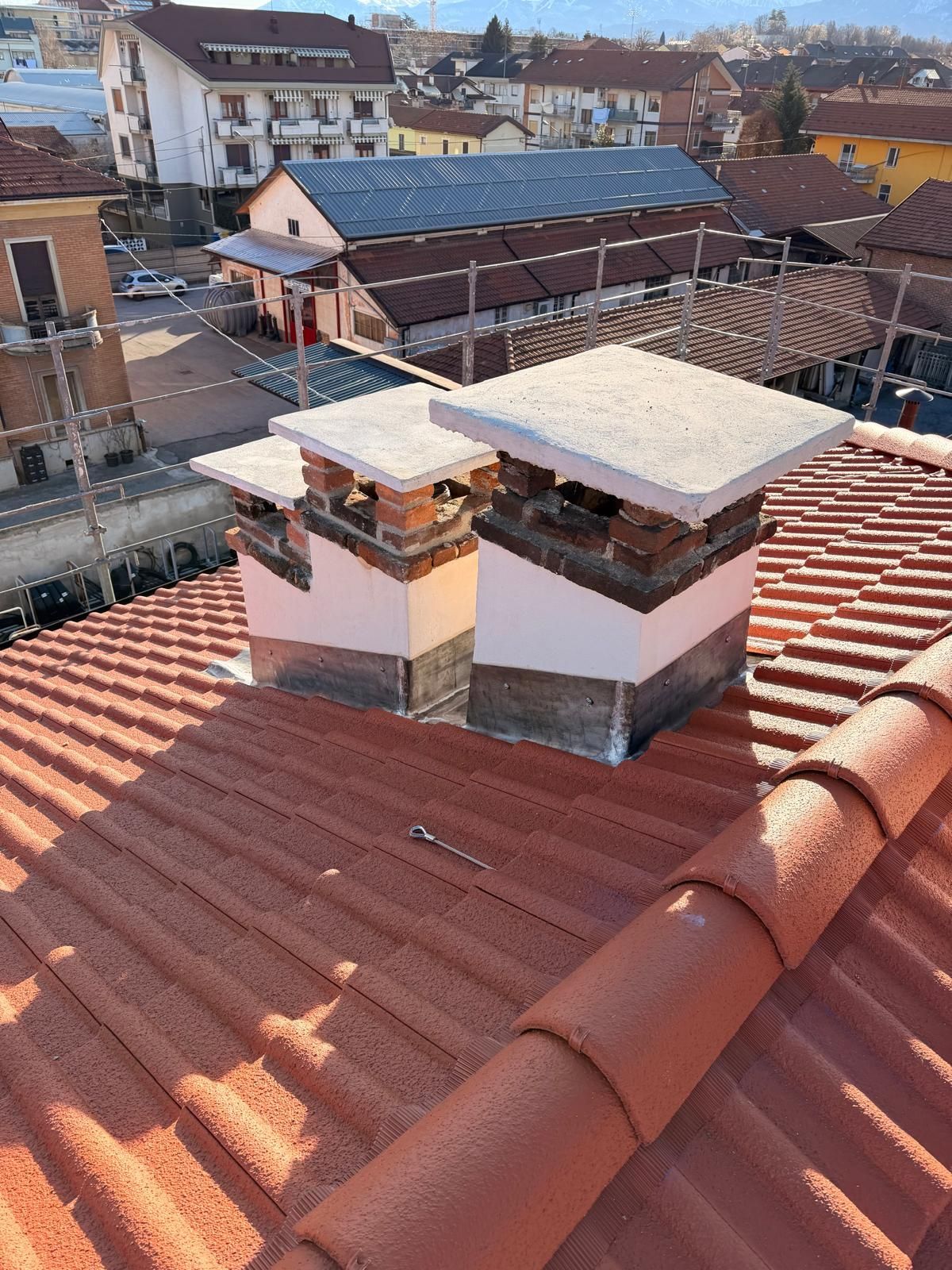 Tetto di tegole rosse con due camini in mattoni, vista della città sullo sfondo.