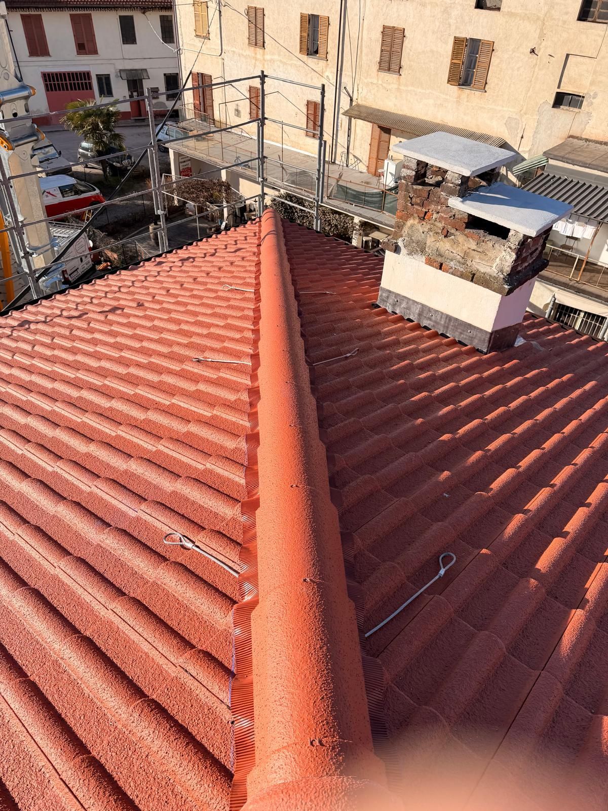 Tetto di tegole rosse con colmo centrale, visto dall'alto, in un contesto urbano.