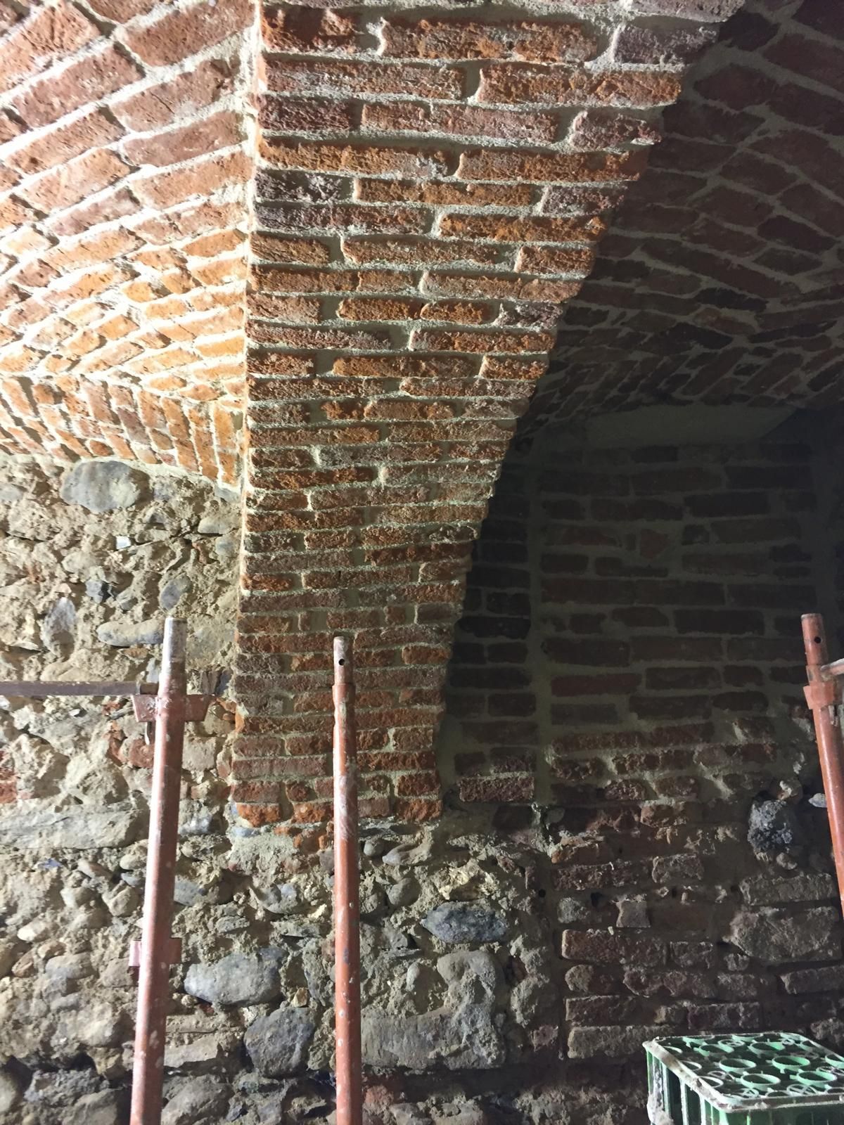 Soffitto ad arco in mattoni in una cantina scarsamente illuminata, sostenuto da pali di metallo.