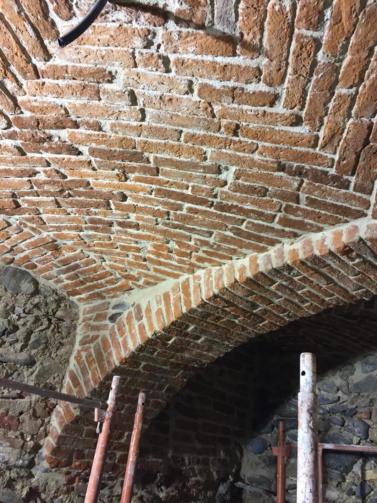 Soffitto a volta in mattoni, sostenuto da impalcature provvisorie, con malta a vista.