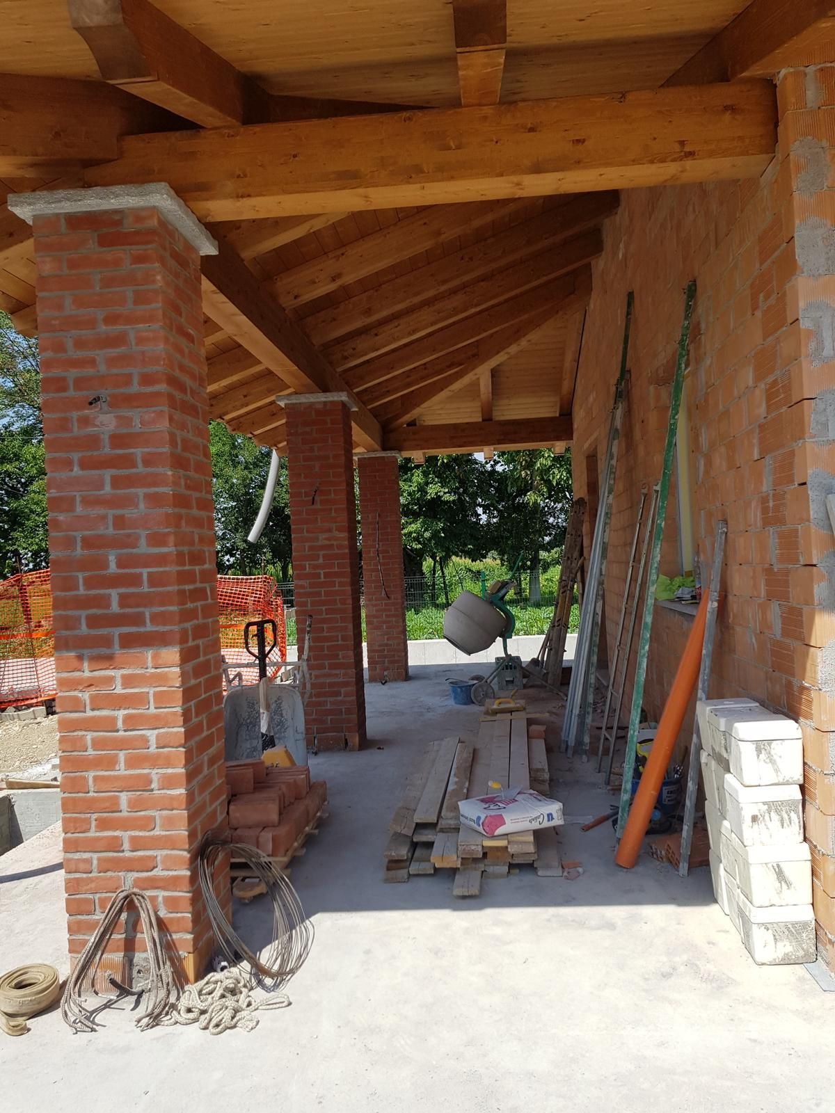Cantiere: pilastri in mattoni che sostengono un tetto in legno. Attrezzi e materiali sono sul pavimento in cemento.