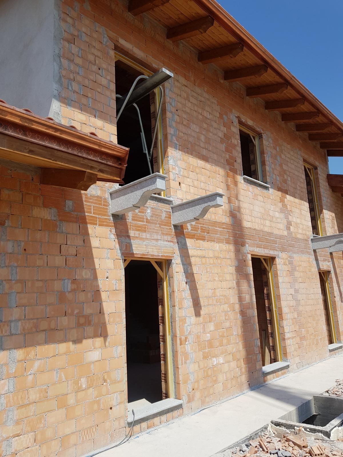 Edificio in mattoni in costruzione, con infissi aperti e sporgenze in cemento.