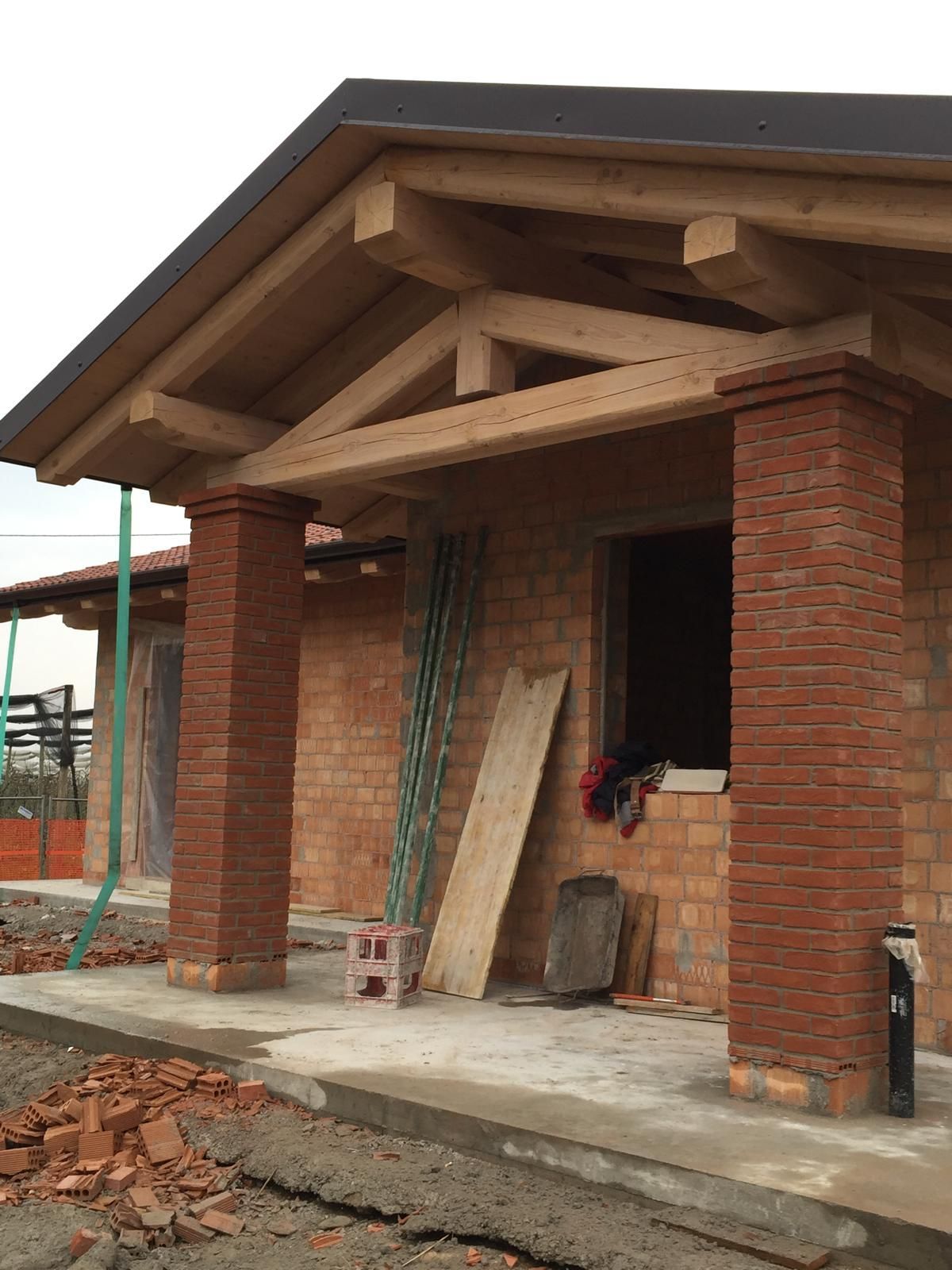 Edificio in costruzione con facciata in mattoni, supporti del tetto in legno e travi a vista.