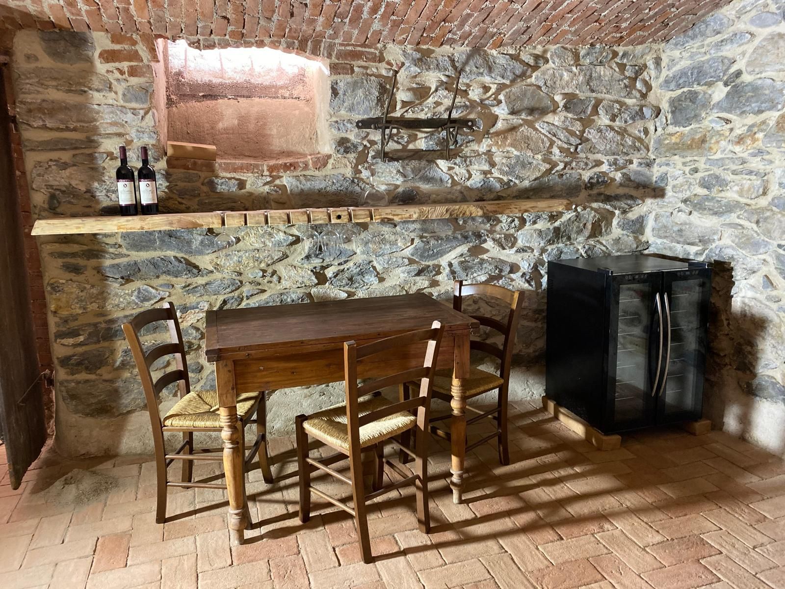 Cantina con pareti in pietra, tavolo e sedie in legno e un piccolo frigorifero.