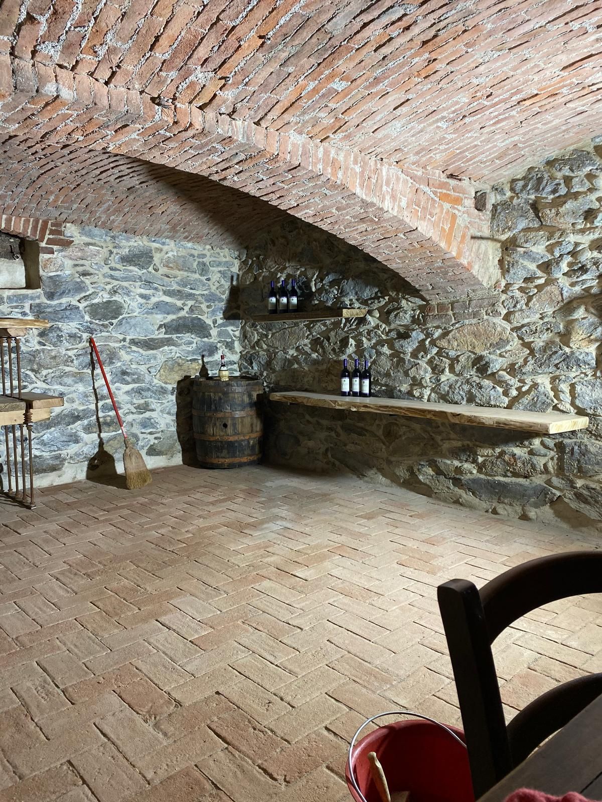 Cantina con soffitto a volta in mattoni, pareti in pietra, pavimento in mattoni, botti, bottiglie sugli scaffali.