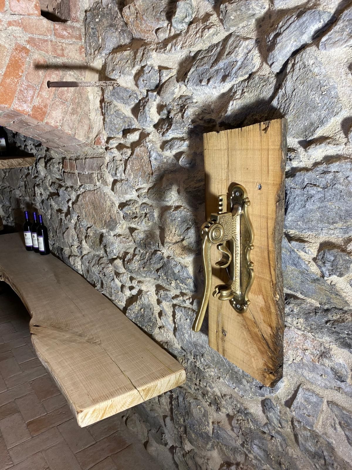 Cantina con tavolo in legno, pareti in pietra e un cavatappi in ottone montato su legno.