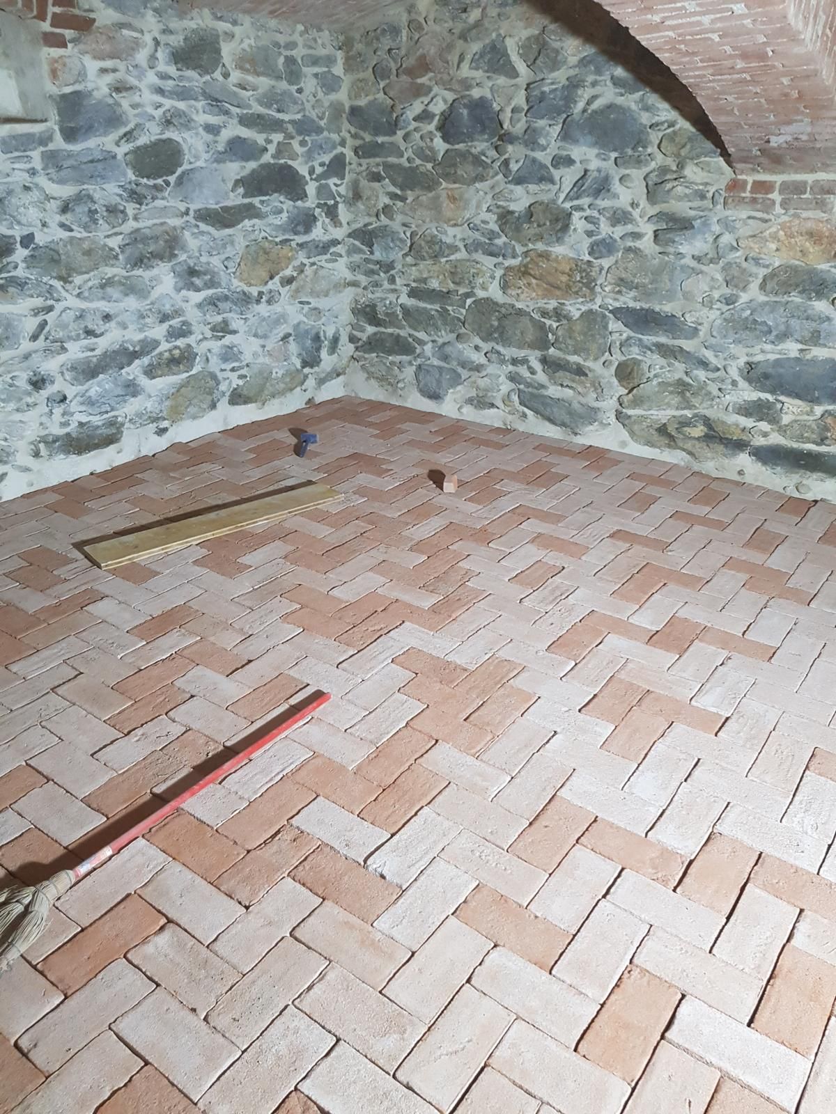 Pavimento in mattoni a spina di pesce in una stanza con pareti in pietra e mattoni.