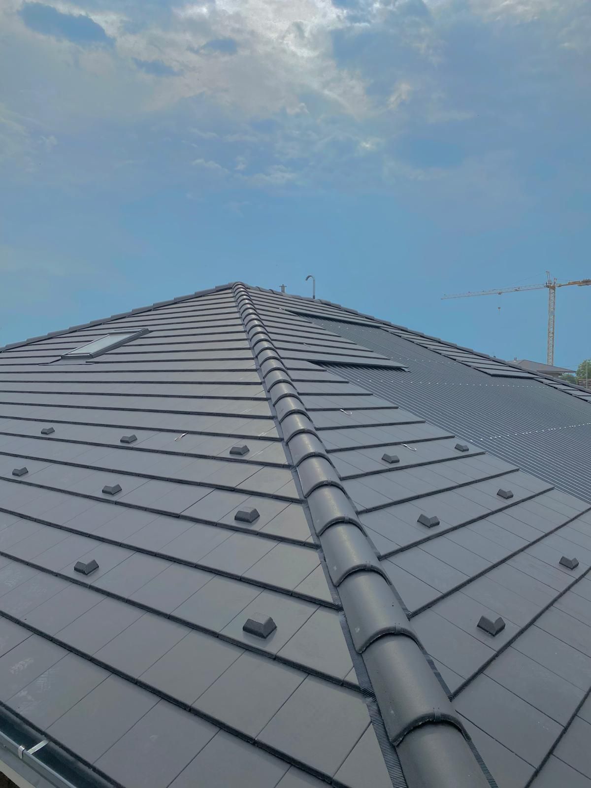 Tetto di tegole grigie con colmo centrale sotto un cielo azzurro nuvoloso.