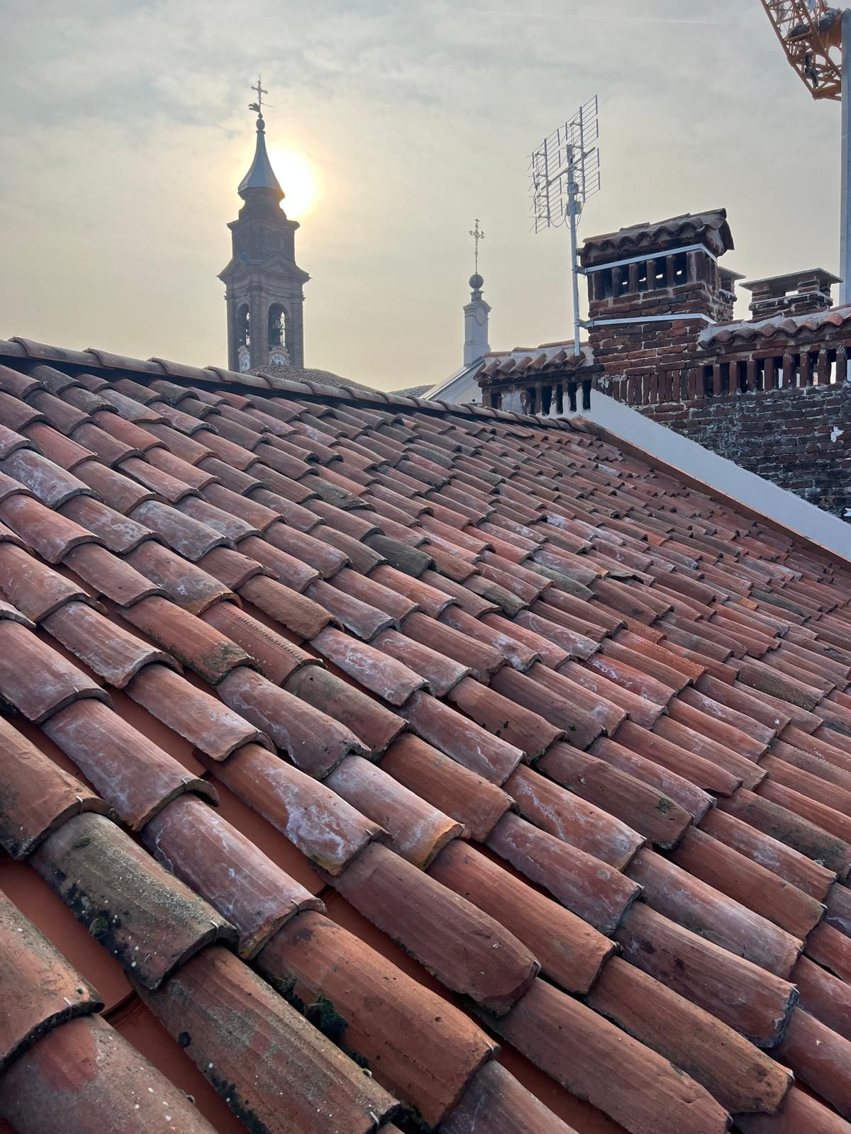 Tetto di tegole rosse con campanile di una chiesa e paesaggio urbano sullo sfondo di un cielo luminoso.