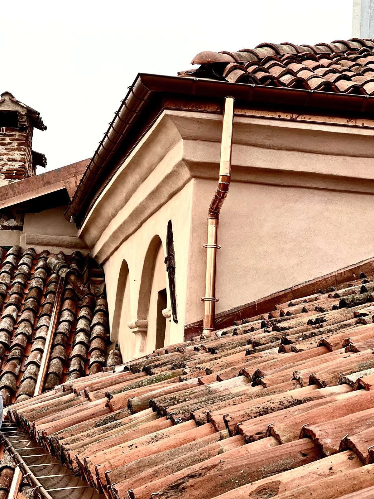 Tetti in tegole di argilla ed edificio color marrone chiaro con finestre ad arco e grondaia in rame.
