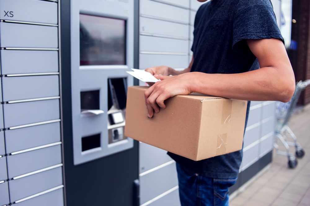 A Man is Holding a Cardboard Box in Front of a Locker — Express Couriers Mackay in Moranbah, QLD