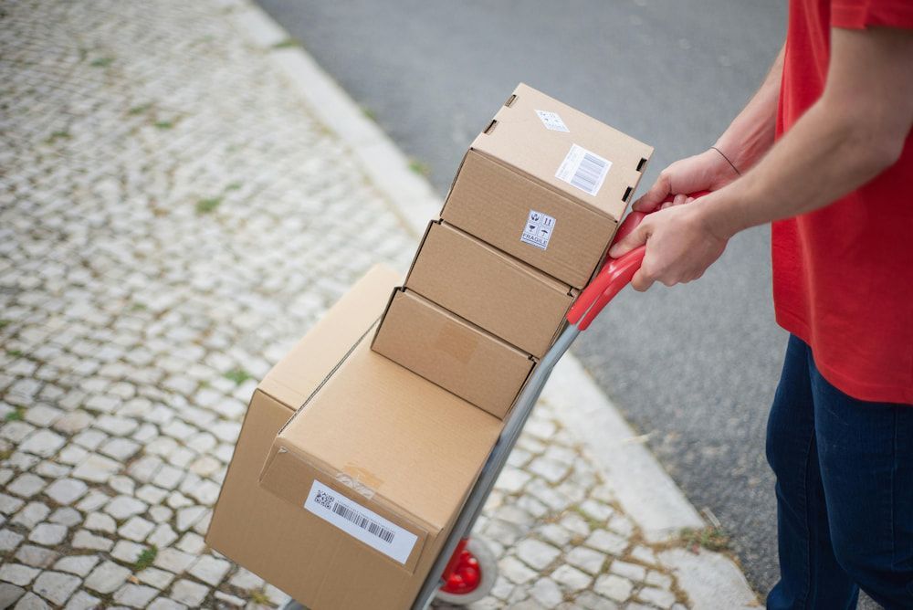 A Man in a Red Shirt is Pushing a Cart With Delivery Packages on It — Express Couriers Mackay in West Mackay, QLD