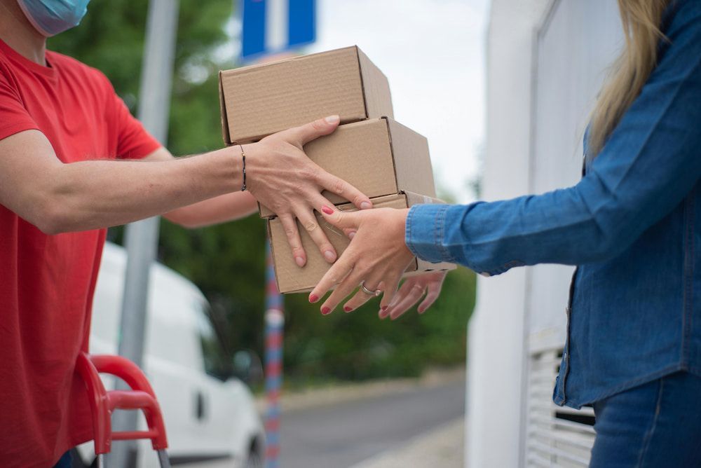 A Delivery Man Wearing a Mask is Handing a Stack of Boxes to a Woman — Express Couriers Mackay in West Mackay, QLD