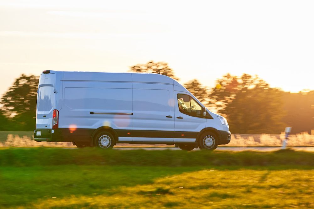 A White Van is Driving Down a Road Next to a Grassy Field — Express Couriers Mackay in Nebo, QLD