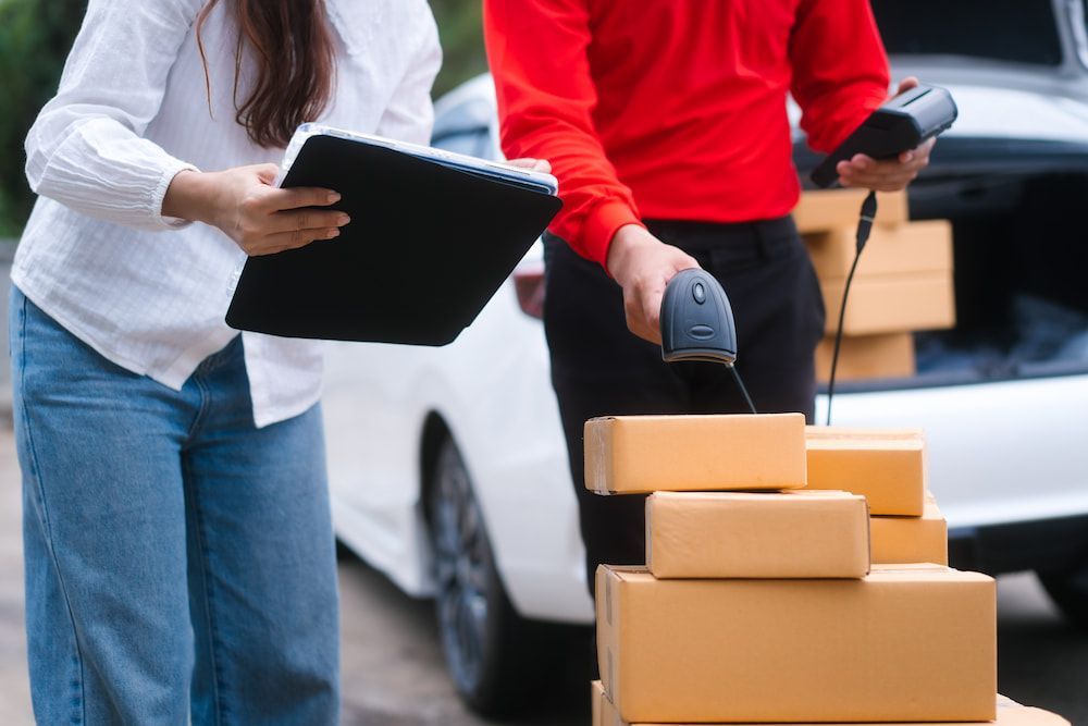 A Delivery Man is Scanning a Stack of Boxes While a Woman Looks on — Express Couriers Mackay in West Mackay, QLD