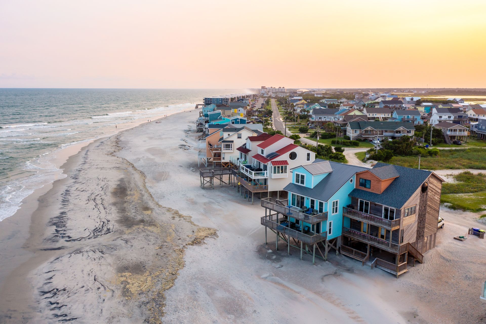An aerial view of a row of colorful houses on stilts on a beach.
