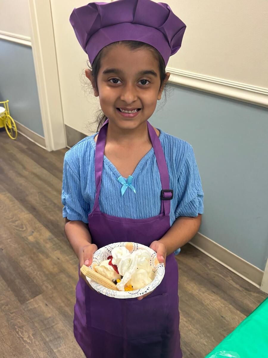 Smiling child in purple chef outfit holding a plate of cookies indoors