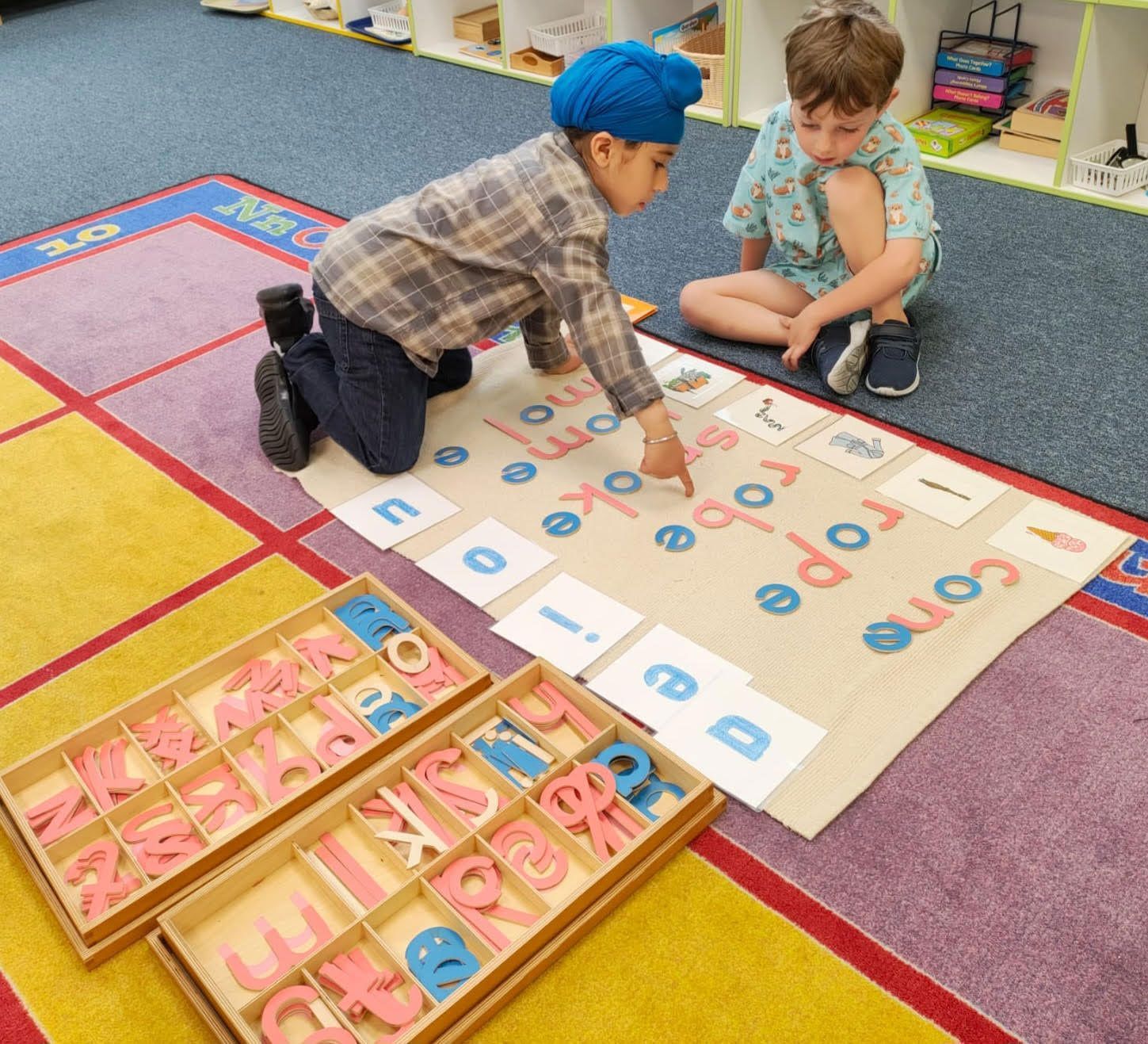two primary Montessori children collaborate on a literacy lesson using the movable alphabet to build words on a work rug.