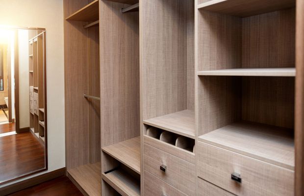 A walk in closet with wooden shelves and drawers and a mirror.