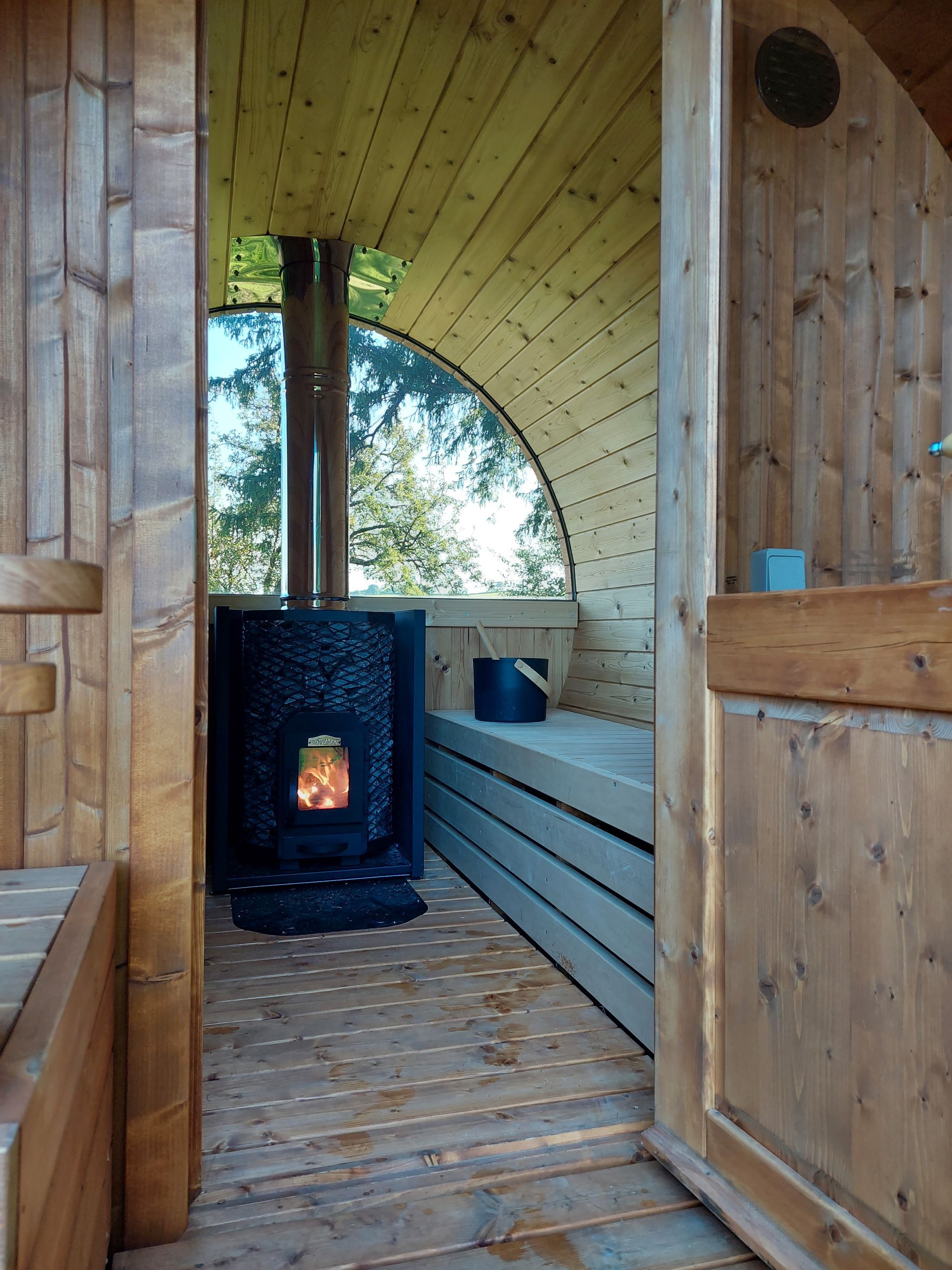 A wooden sauna with a stove in the middle of it.