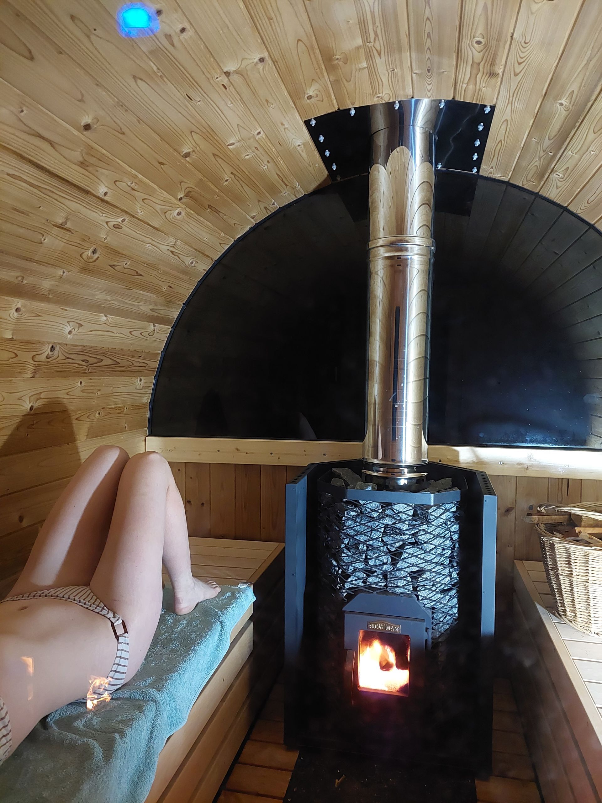 A woman is laying in a sauna next to a stove.