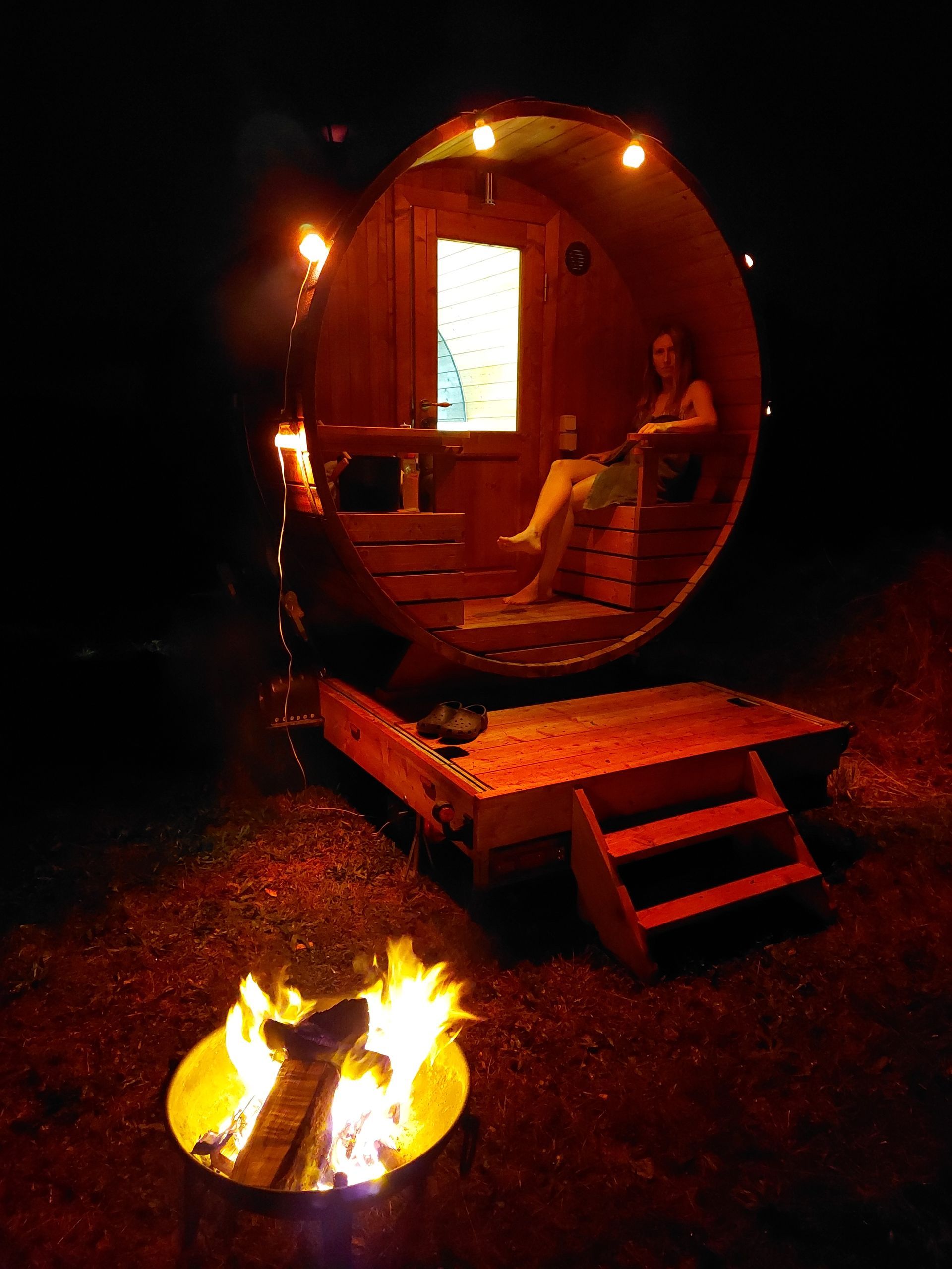 A woman is sitting in a barrel next to a fire pit