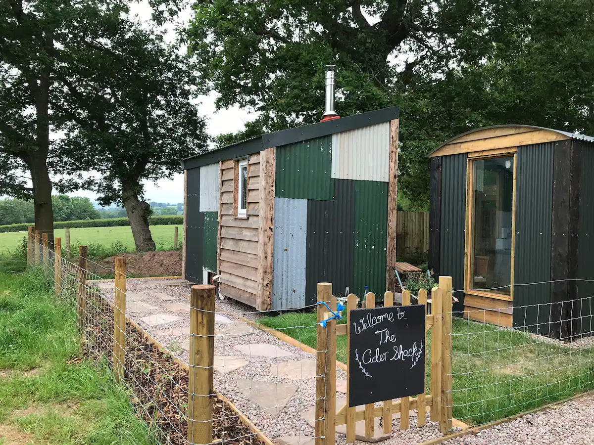 A small house is sitting in the middle of a field next to a fence.