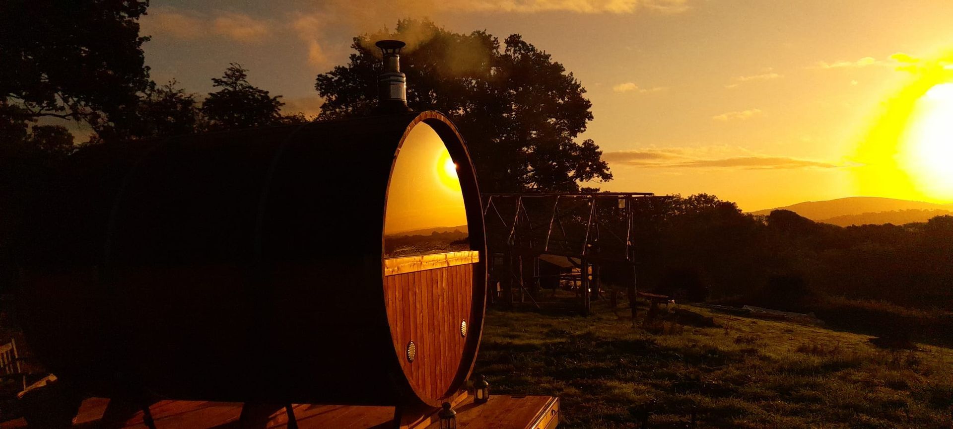 A wooden barrel is sitting in the middle of a field at sunset.