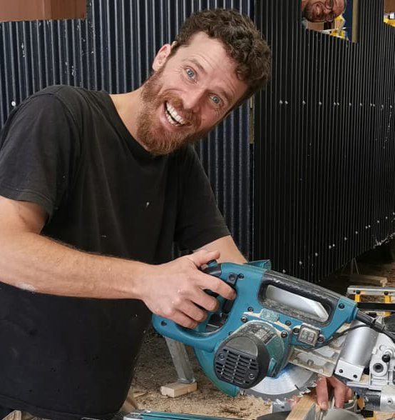 A man with a beard is smiling while holding a circular saw
