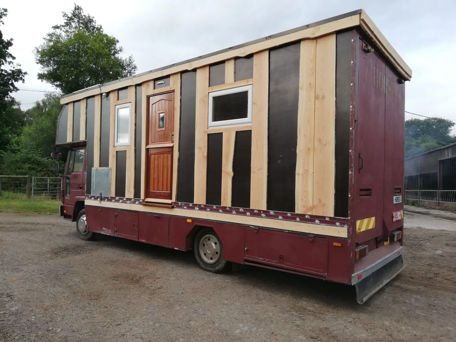 A red truck with a wooden roof is parked in a gravel lot